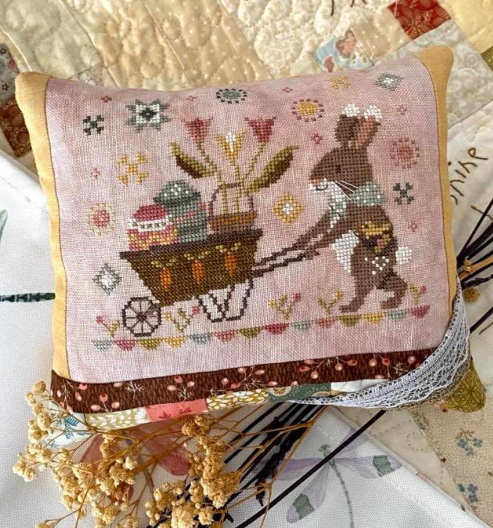 Embroidered pillow with a bunny delivering an Easter basket, on a textured surface.