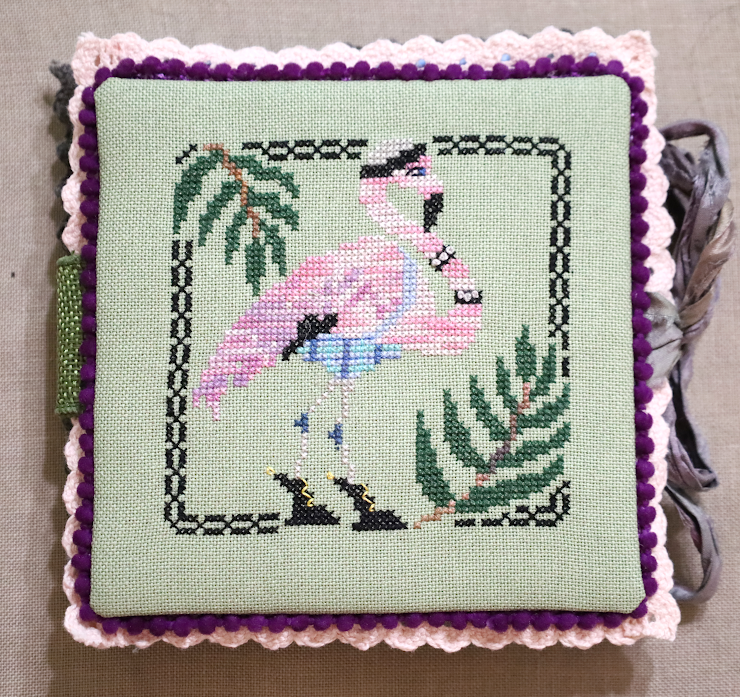 Cross-stitched flamingo design on a green background with decorative border