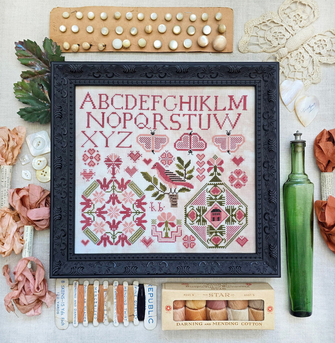 Framed cross-stitch pattern with embroidery supplies on a textured surface
