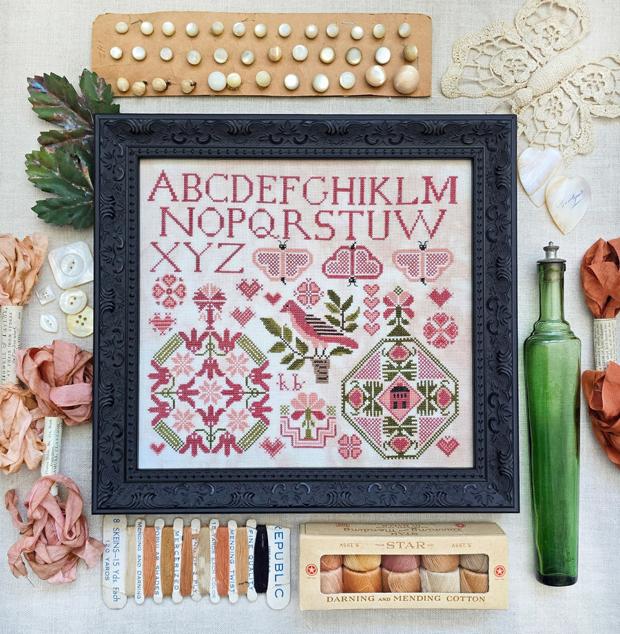 Framed cross-stitch pattern with embroidery supplies on a textured surface