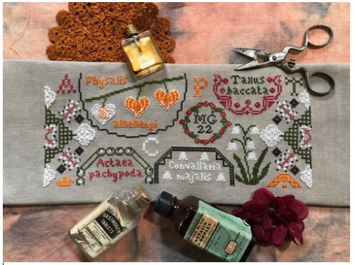 Cross-stitched design on fabric with decorative items like a bottle, scissors, and flowers.