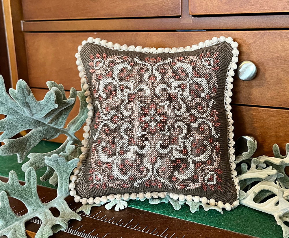 Decorative pillow with intricate pattern on a wooden surface with decorative plants.