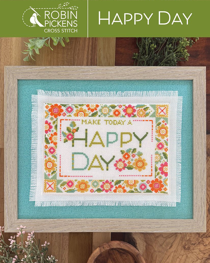 Cross-stitched design with 'Make Today a Happy Day' text on a wooden surface with plants.