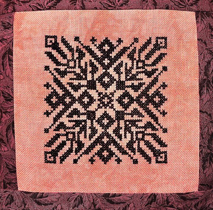 geometric deisgn with dark thread on coral-y fabric