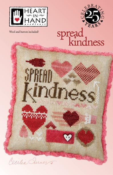 Cross-stitched pillow with 'Spread Kindness' text and red hearts on a pink background, featuring Heart in Hand branding.