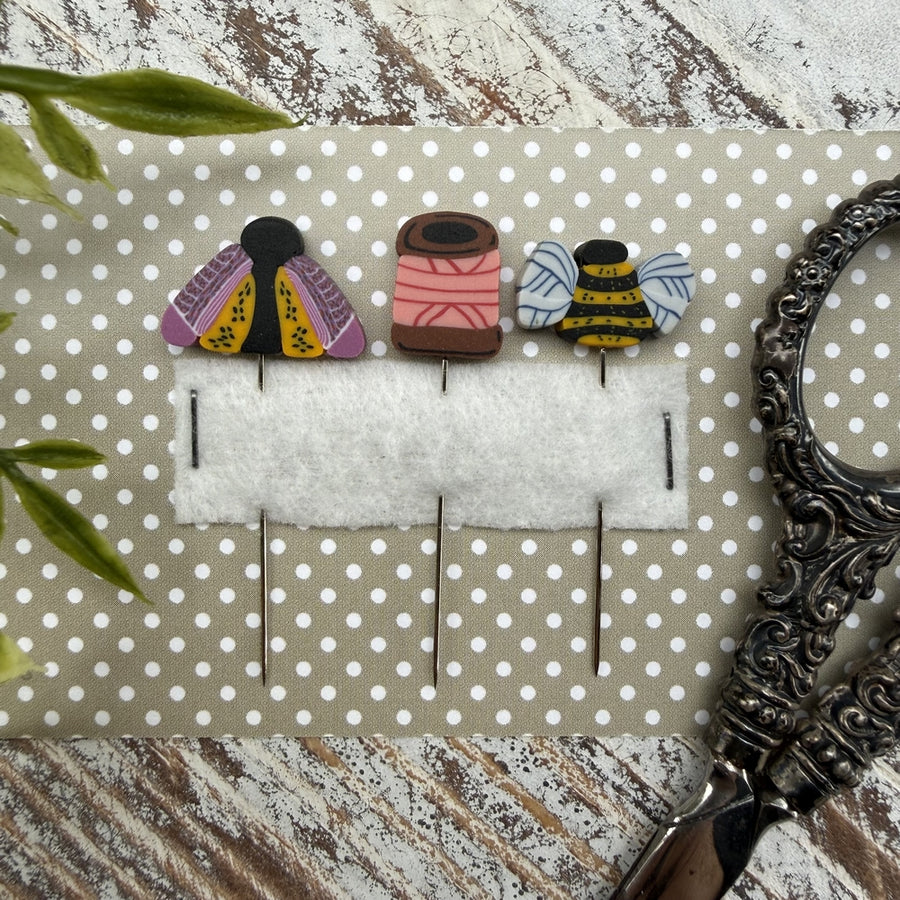 Three colorful brooches on a polka dot card with a decorative frame and scissors in the background.