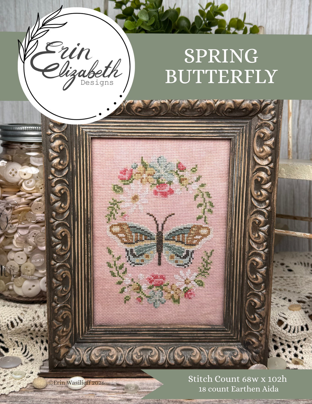 Framed cross-stitched butterfly design with floral elements on a pink background, featuring Erin Elizabeth Designs.