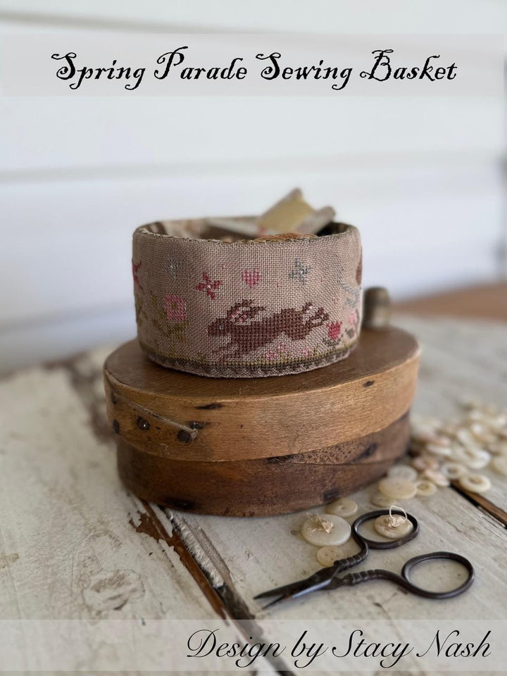 Sewing basket with a fabric roll and scissors on a wooden surface, labeled 'Spring Parade Sewing Basket' by Stacy Nash.