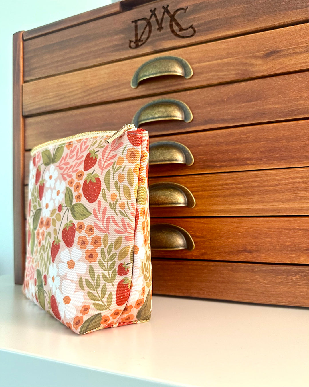 Floral-patterned pouch in front of a wooden drawer with brass handles.