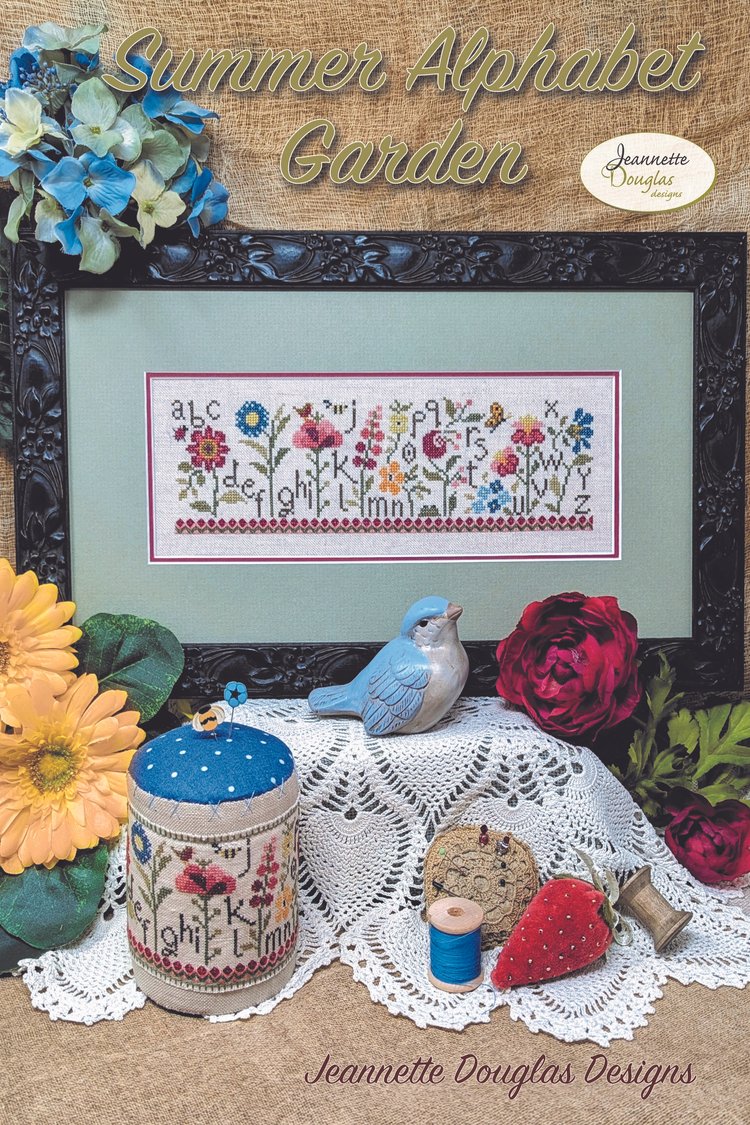 Cross-stitch pattern with floral design and decorative items on a lace tablecloth.