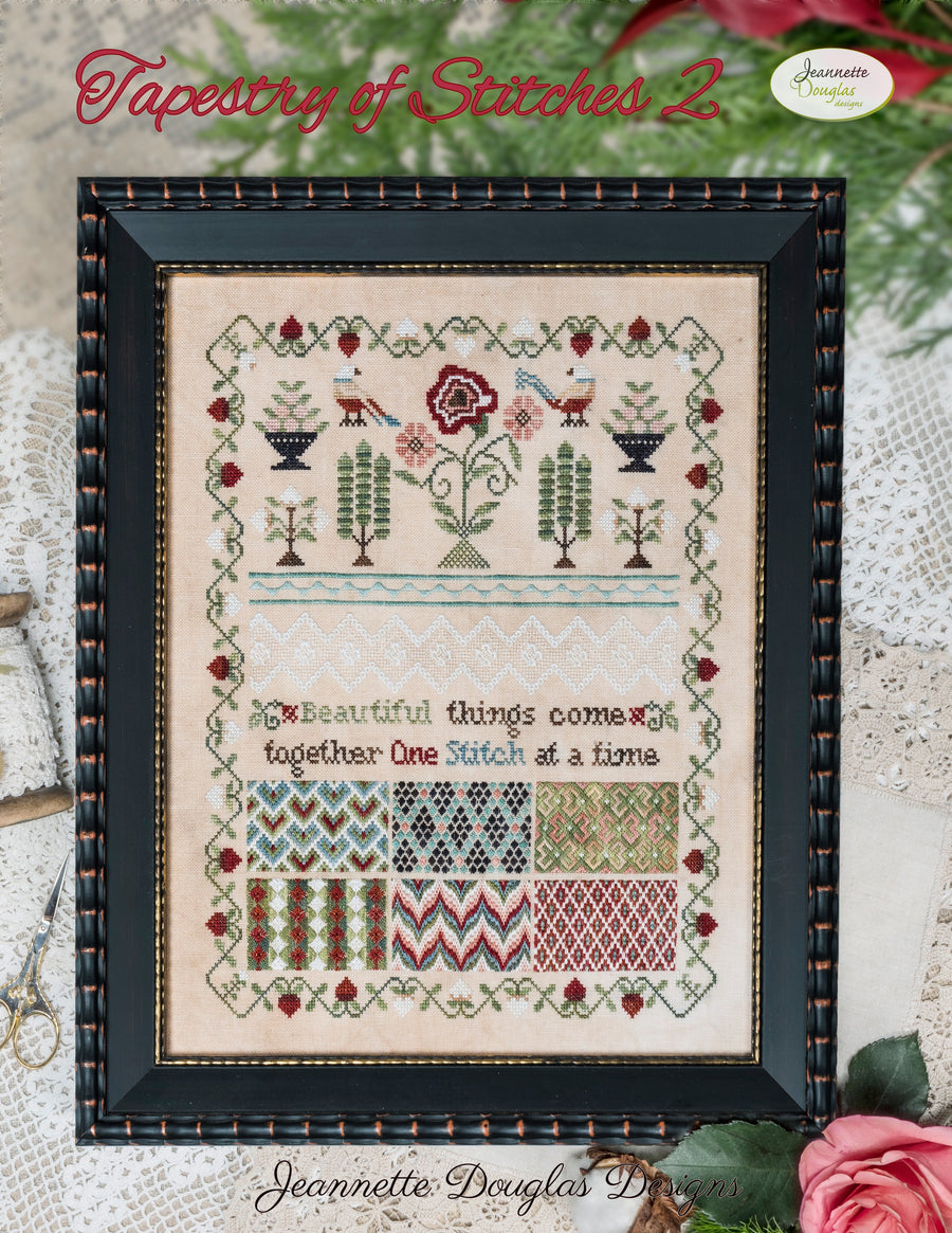 Framed cross-stitch pattern with decorative elements on a textured surface.