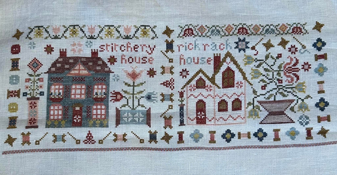 Cross-stitched design of two houses with decorative elements on a white background, featuring the 'Stitchery Rick Rack House' brand.