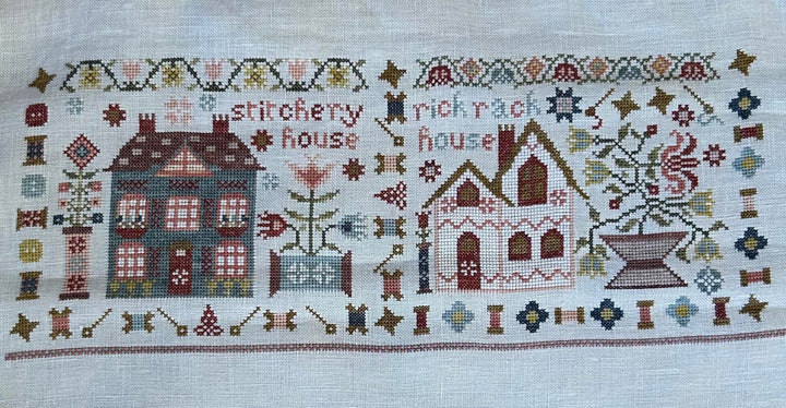 Cross-stitched design of two houses with decorative elements on a white background, featuring the 'Stitchery Rick Rack House' brand.