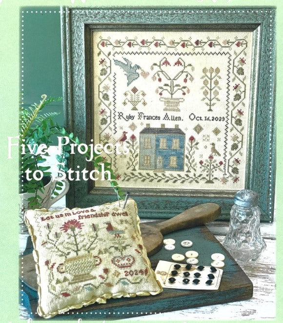 Framed cross-stitched artwork on a table with decorative items