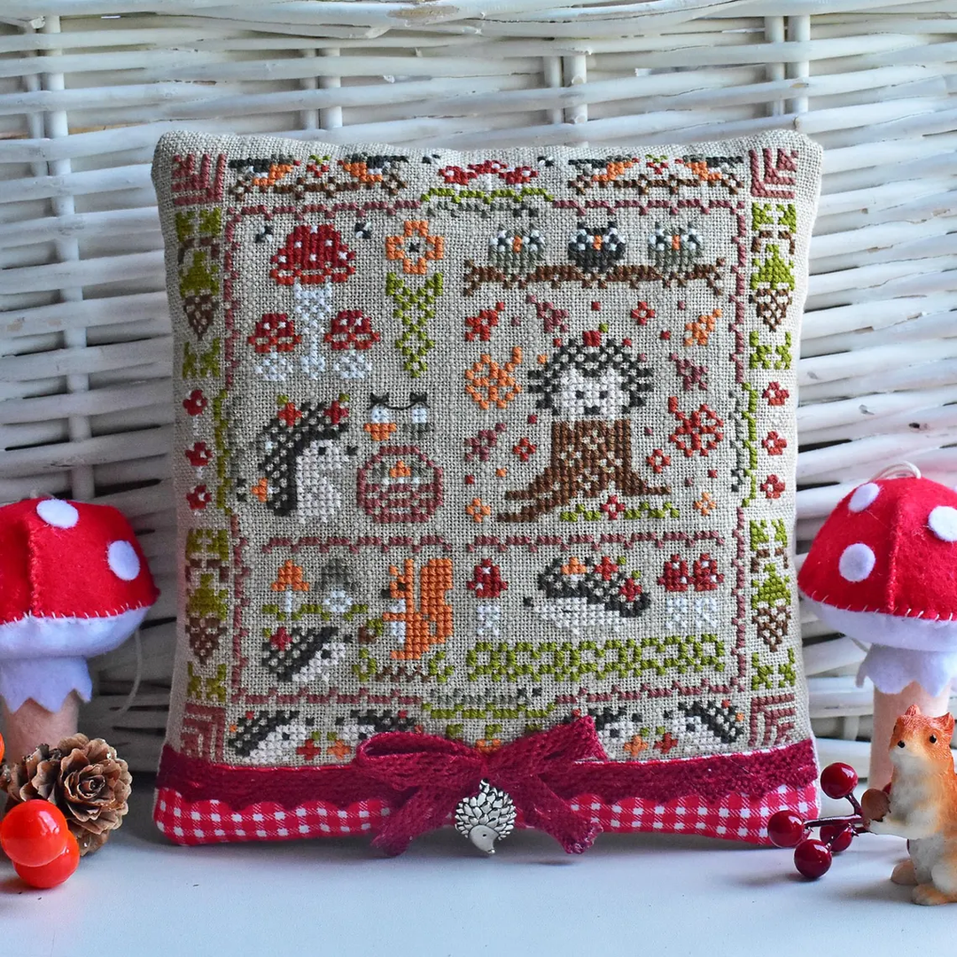 Decorative pillow with cross-stitch design featuring animals and nature elements, surrounded by small decorative items.