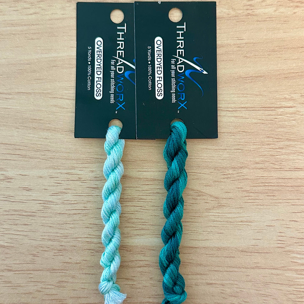 Two teal twisted thread skeins ThreadworX cards against a wooden surface