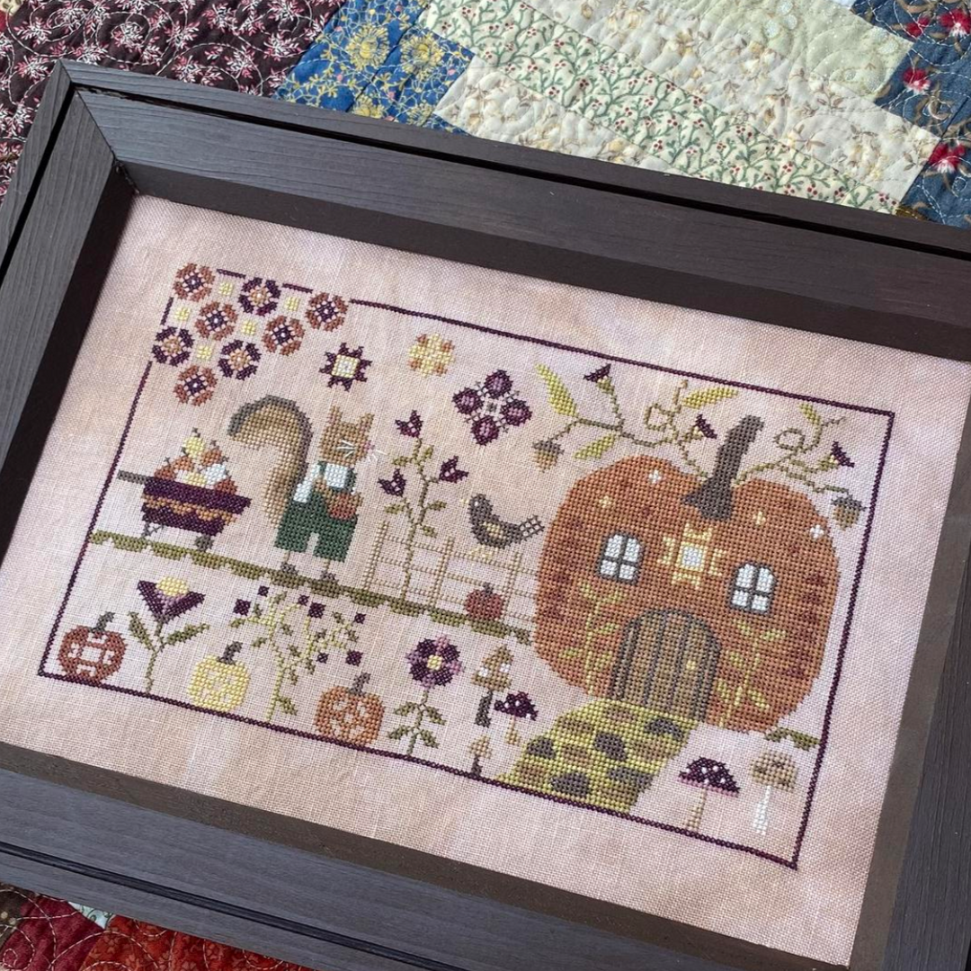 Framed cross-stitched piece titled 'Tommy's Pumpkin Patch' on a quilted background.