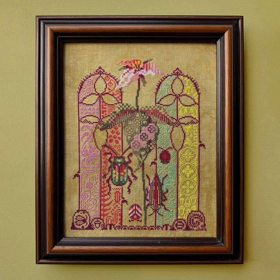 Framed cross-stitched artwork on a beige background