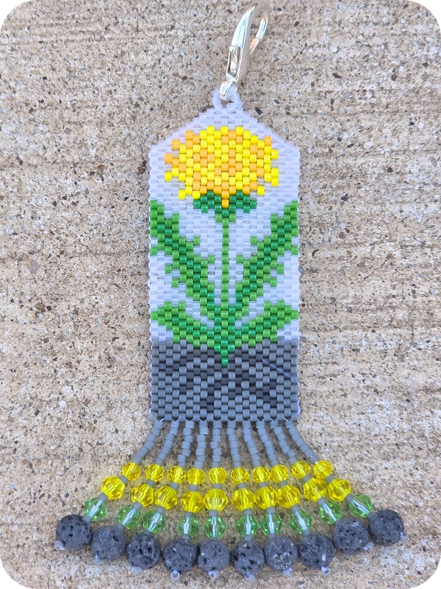 Beaded pendant with a yellow flower design on a textured surface