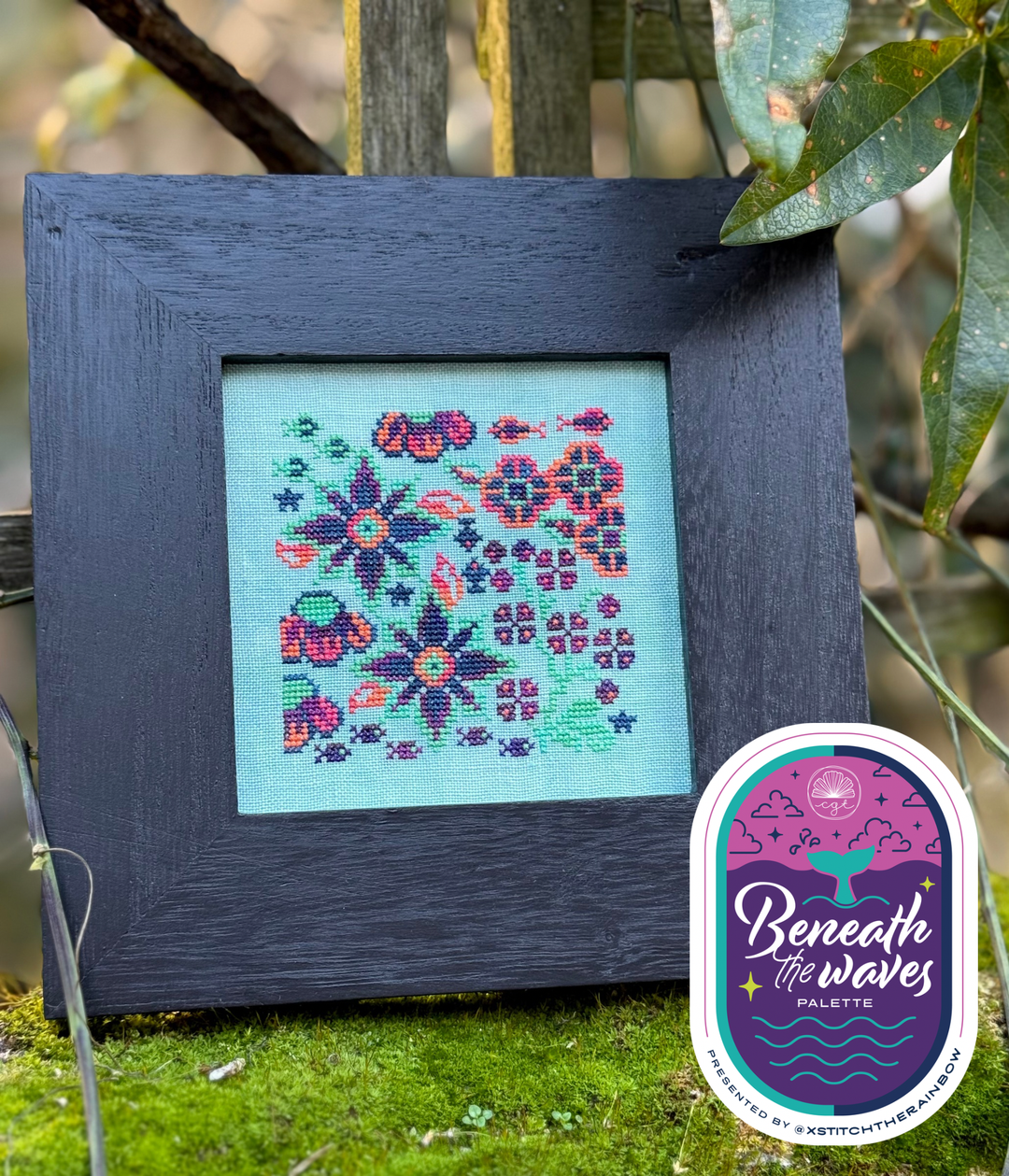 Framed cross-stitched floral design with 'Beneath the Waves' palette logo.
