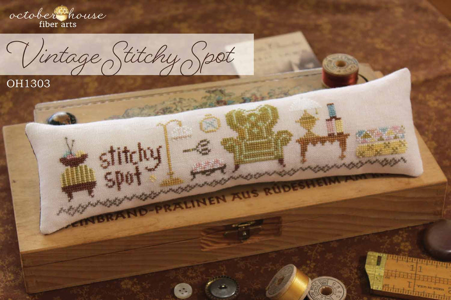 Cross-stitched pillow with 'stitchy spot' text on a wooden box, surrounded by sewing supplies.