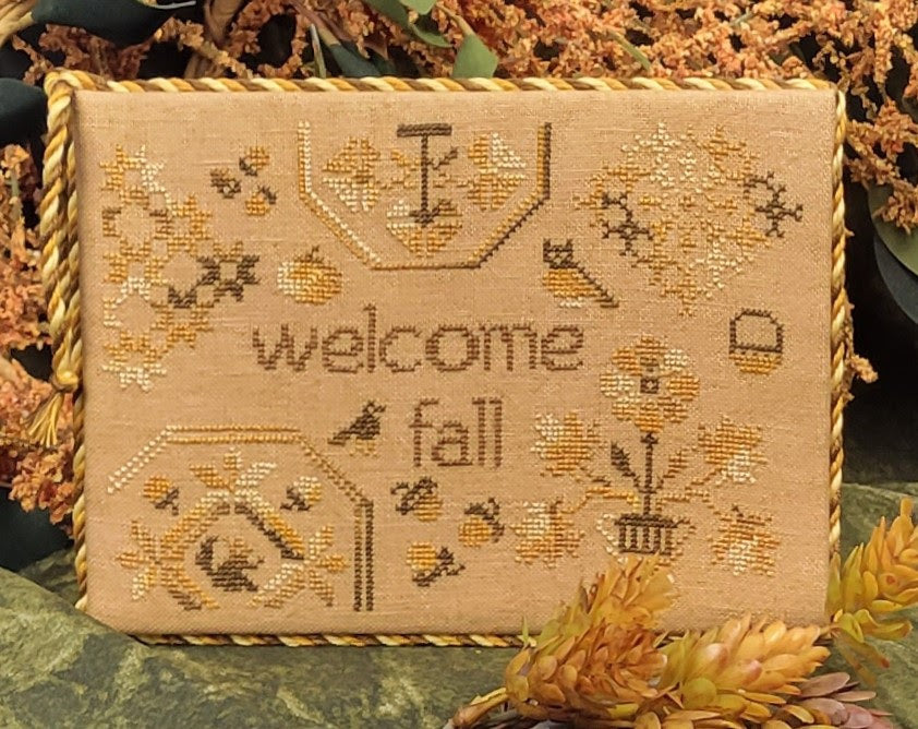 Embroidered fabric with 'welcome fall' text surrounded by autumn-themed decorations.