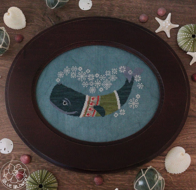 Embroidery of a whale wearing a sweater on a wooden surface with decorative items.