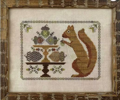 Cross-stitched design of a squirrel and a cake stand on fabric with a wooden frame.