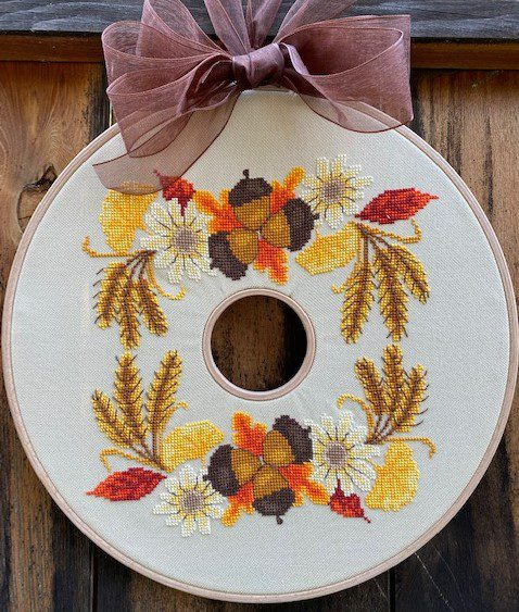 Embroidery hoop with autumn-themed floral design and a pink bow on a wooden background