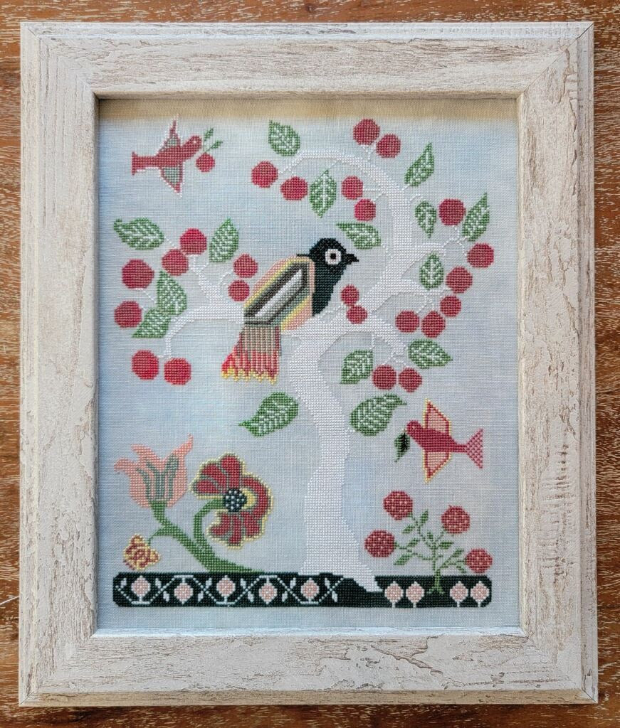 Framed cross-stitched piece with birds and berries on a light blue background