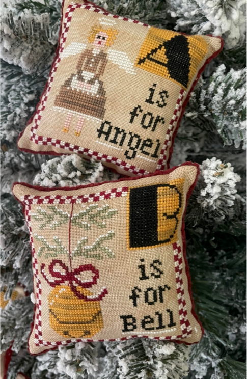 Two embroidered pillows with Christmas-themed designs on a tree.