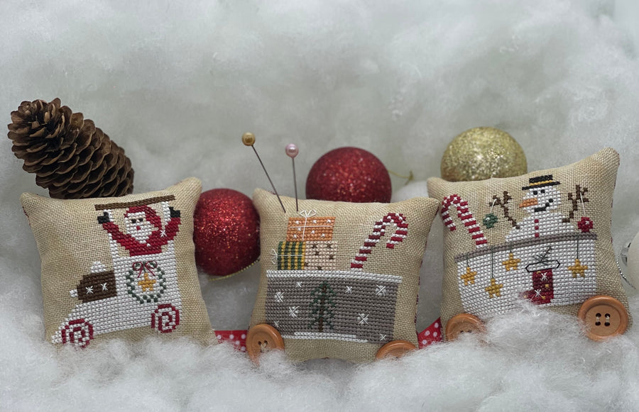Three cross-stitched Christmas-themed cushions on a snowy background
