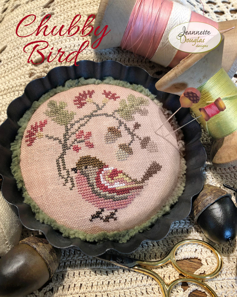 Embroidered pin cushion with a bird design surrounded by sewing supplies on a textured fabric background.