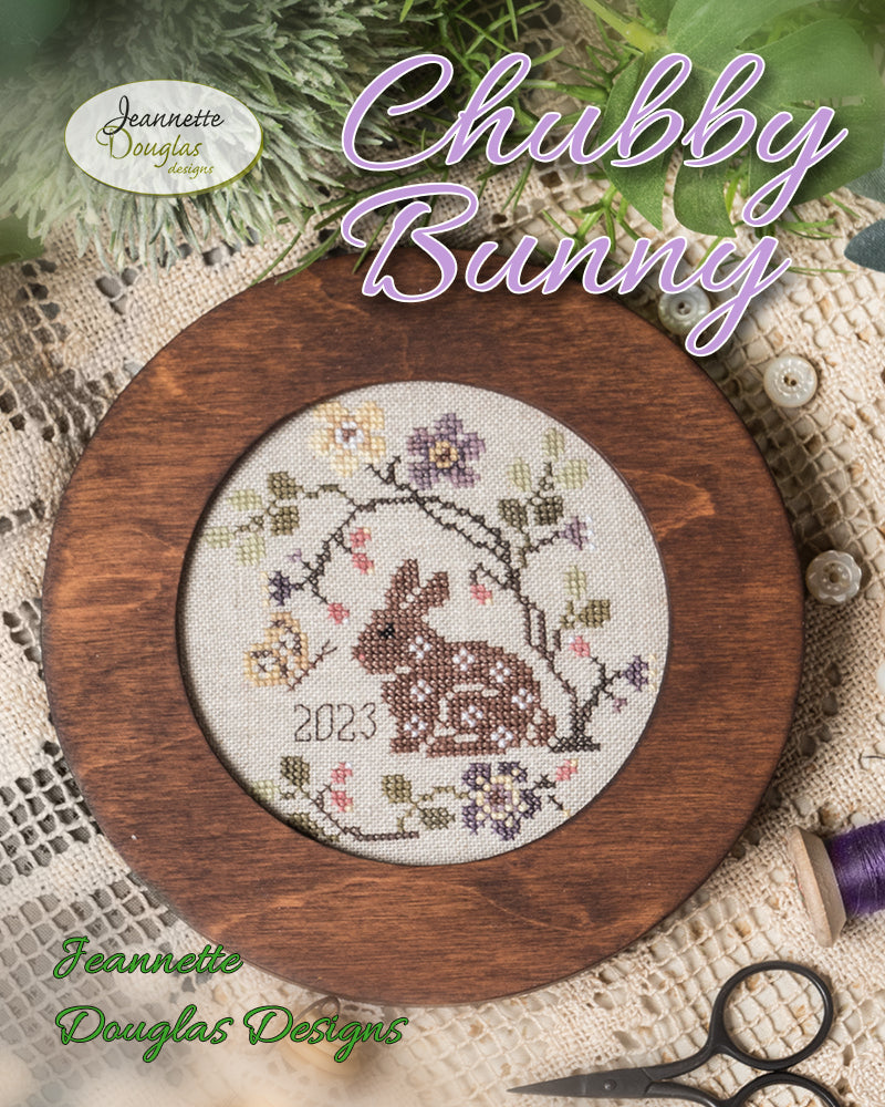 Cross-stitched bunny design in a wooden frame with 'Chubby Bunny' text and 'Jeannette Douglas Designs' branding.