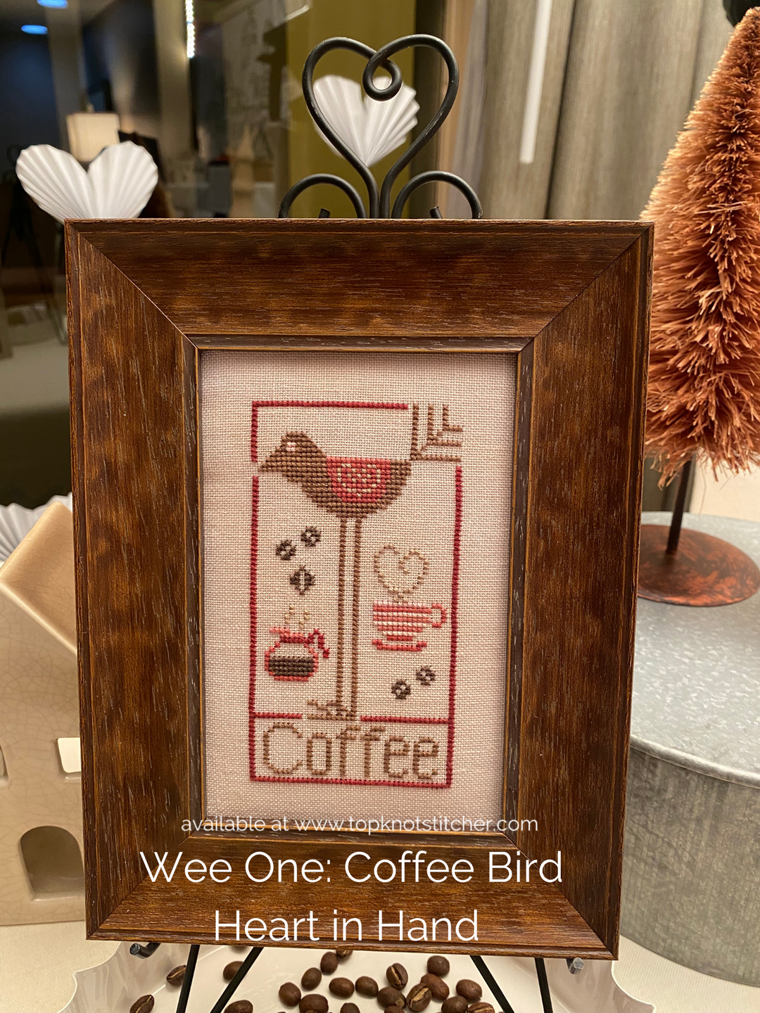 Framed cross-stitched artwork with a coffee-themed design on a table.