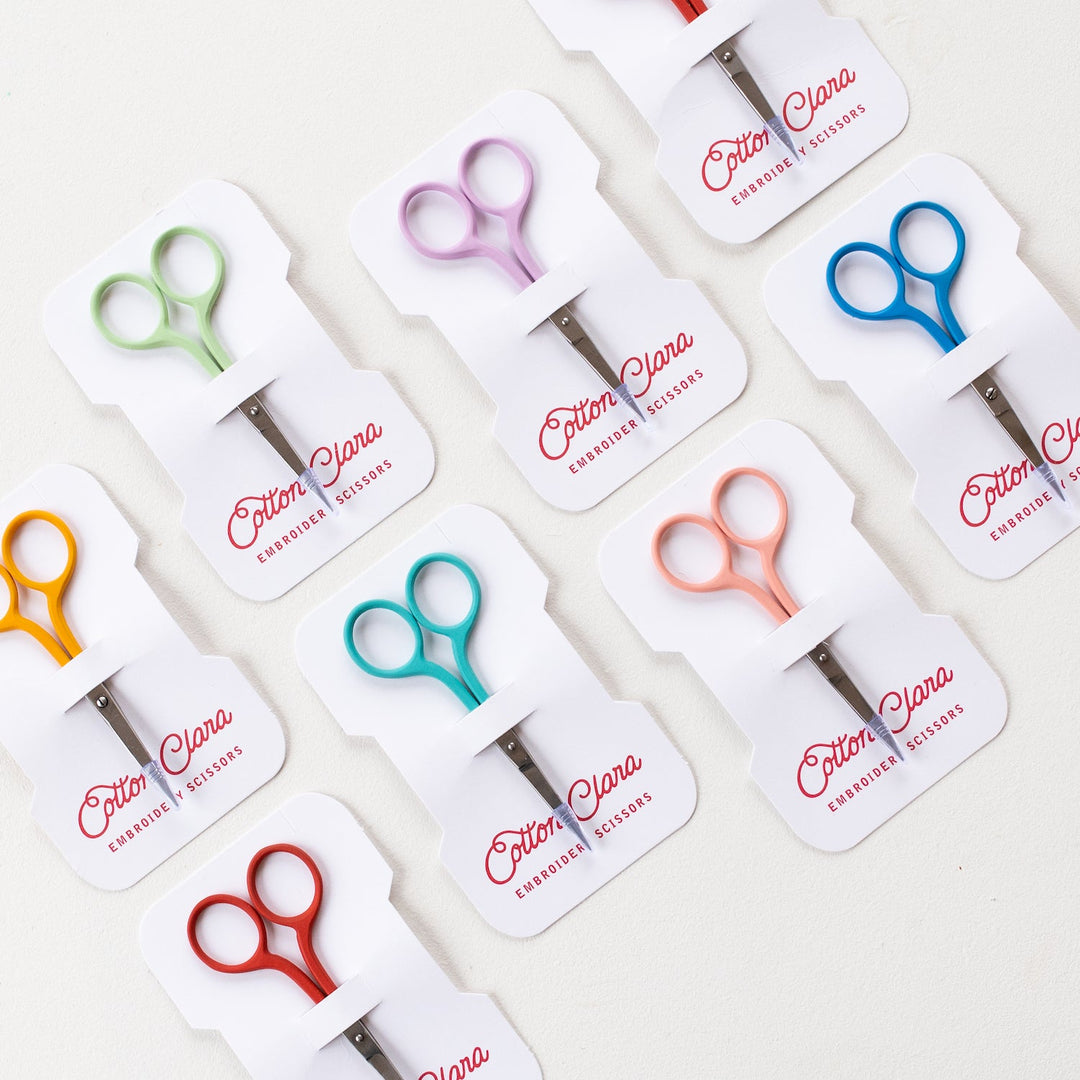 Set of colorful scissors in their packaging with 'Cotton Clara' branding on a white background.