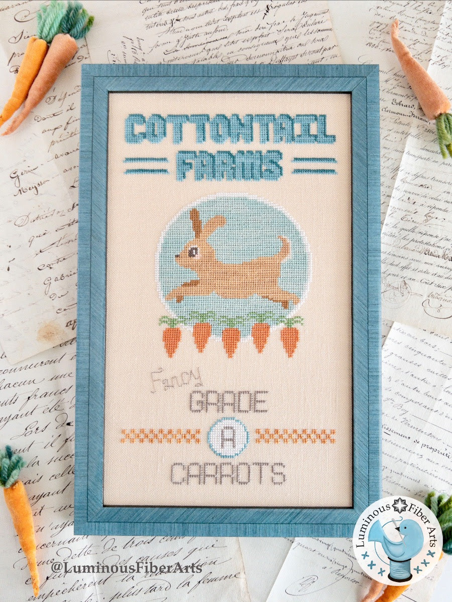 Cross-stitched design of a bunny and carrots with 'Cotton Tail Farms' text on a textured paper background.