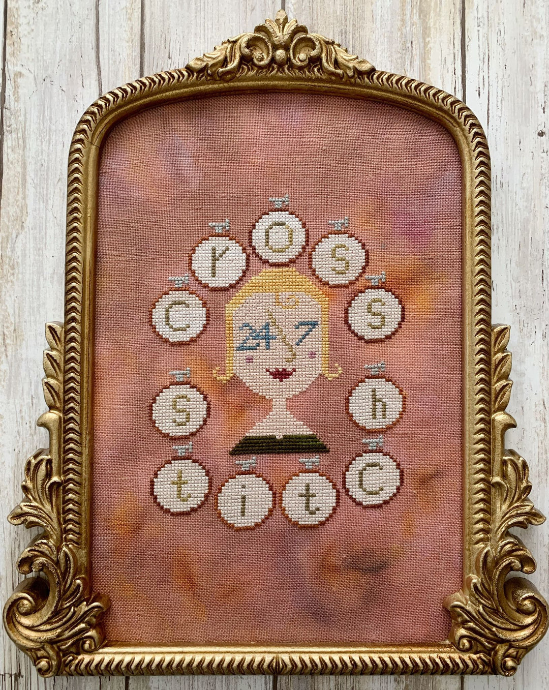 Framed cross-stitched artwork with decorative elements on a wooden background