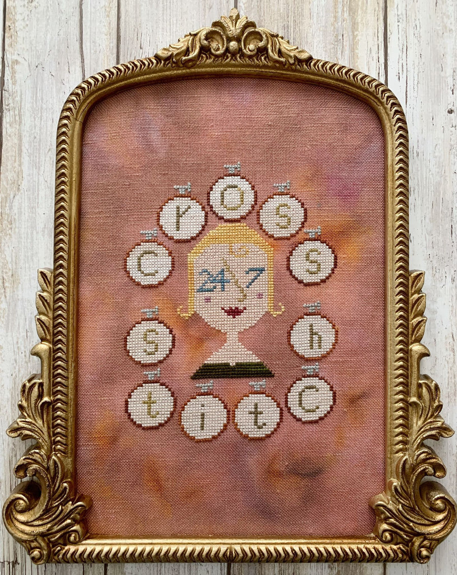 Framed cross-stitched artwork with decorative elements on a wooden background