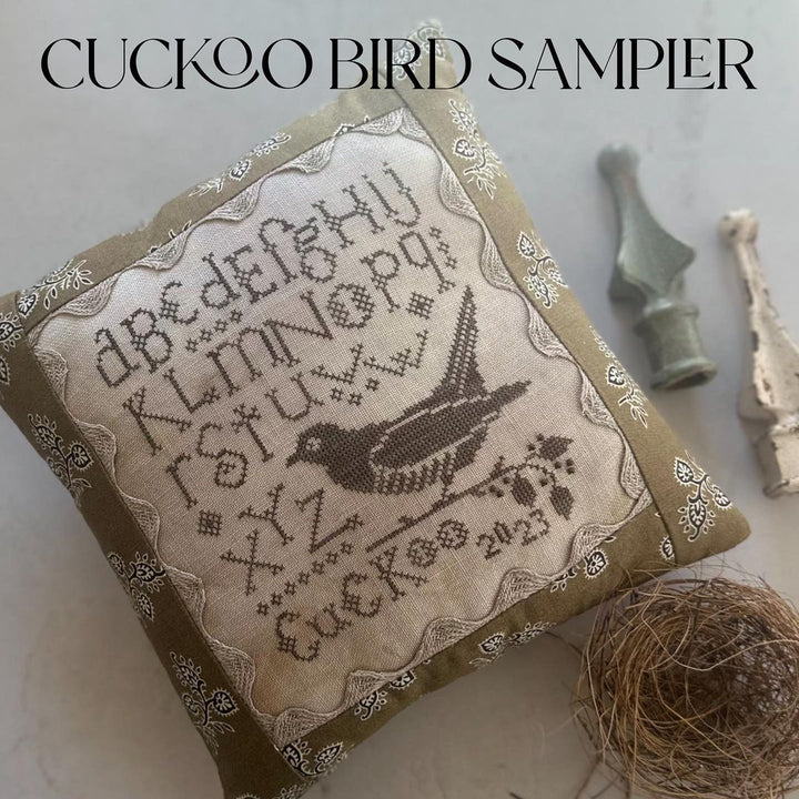 Cuckoo Bird Sampler with cross-stitch design and bird illustration on a textured surface.