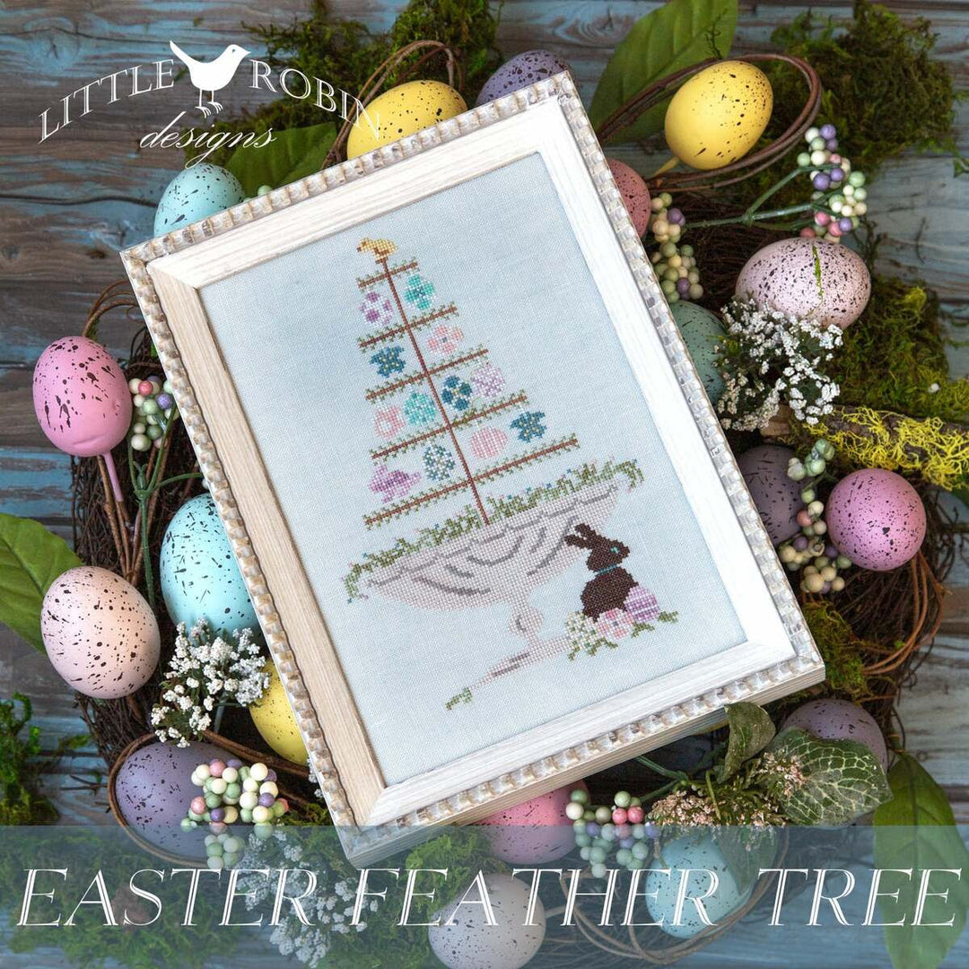 Framed Easter-themed cross-stitch with decorative eggs and greenery on a wooden surface.