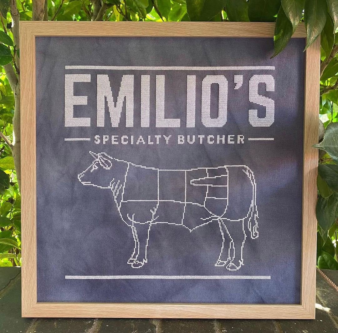 A chalkboard-style pattern with the text 'Emilio's Specialty Butcher' and an illustration of a cow, indicating a design for a butcher shop.