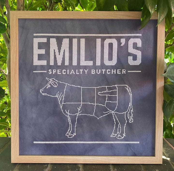 A chalkboard-style pattern with the text 'Emilio's Specialty Butcher' and an illustration of a cow, indicating a design for a butcher shop.