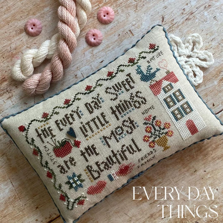 A hand-stitched rectangular pillow with text and embellishments, placed on a wooden surface with a rope and buttons nearby.
