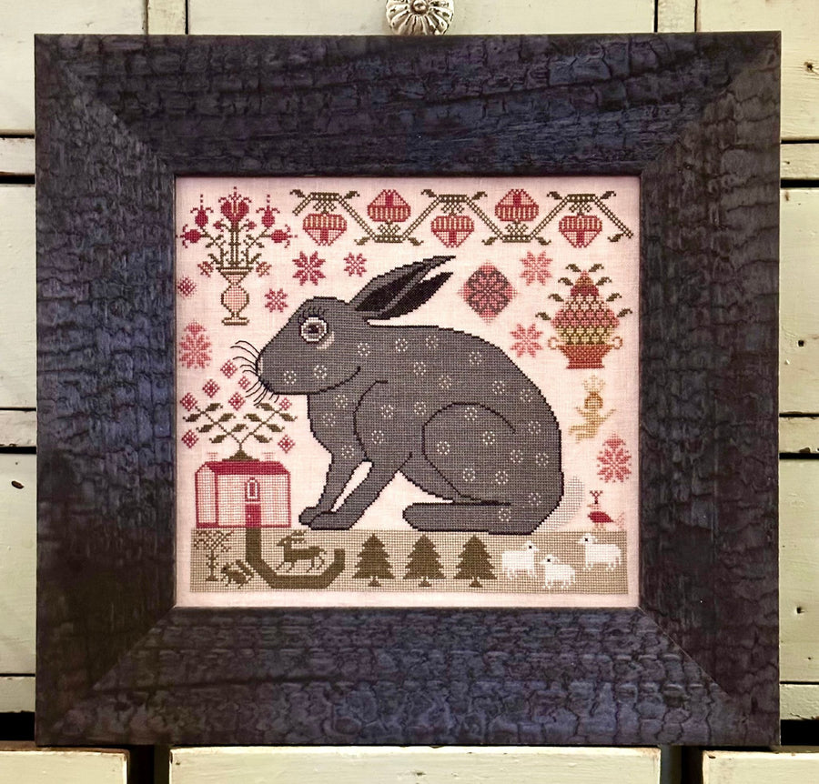 Framed cross-stitched picture of a rabbit with decorative elements on a wooden background