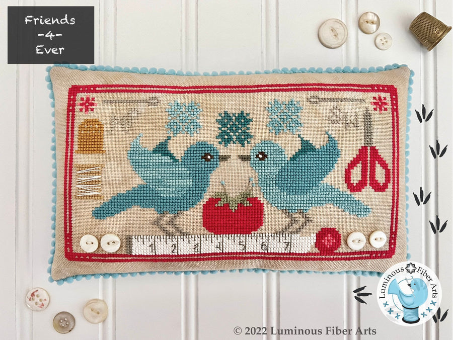 Cross-stitched pillow with two blue birds, a red tomato, and a pair of scissors on a white background.