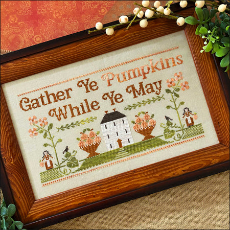 Framed cross-stitched piece with 'Gather Ye Pumpkins While Ye May' text and autumn-themed design.