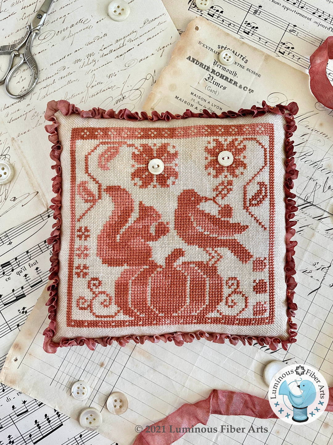 Embroidered pillow with red design on a sheet of music with sewing tools and buttons.
