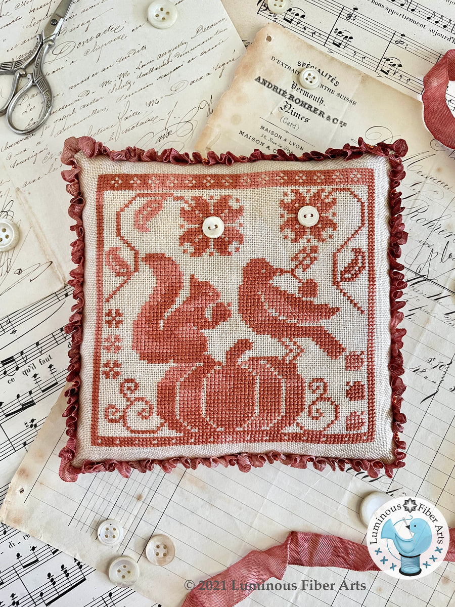 Embroidered pillow with red design on a sheet of music with sewing tools and buttons.