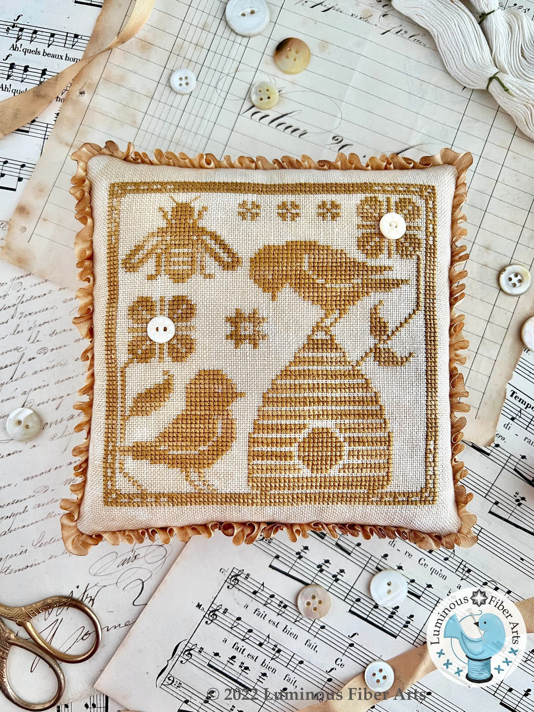 Embroidered square with bees and a beehive on a surface with buttons and thread